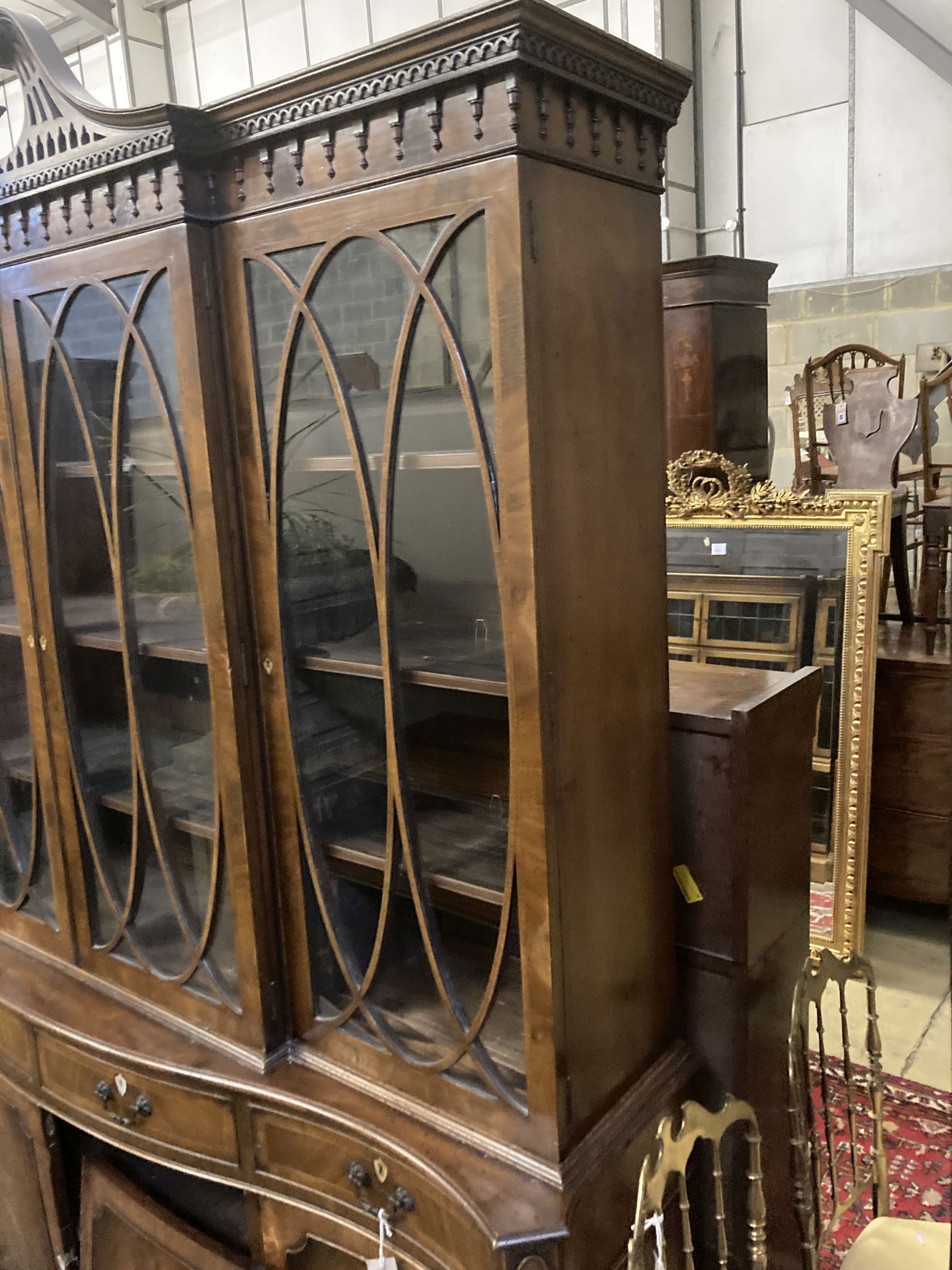 A George III style mahogany and walnut banded breakfront bookcase, with pierced broken swan neck pediment over oval glazing bars,